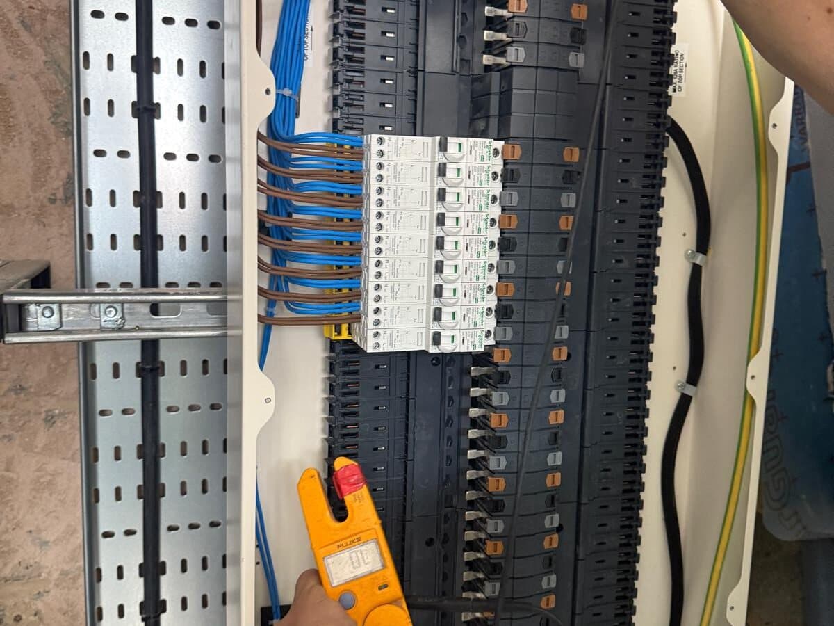 Electrician testing a commercial distribution board with a clamp meter